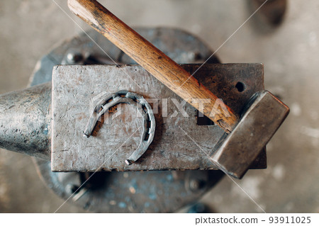 Blacksmith's hammer and horseshoe on metal anvil at forge. Overhead view 93911025