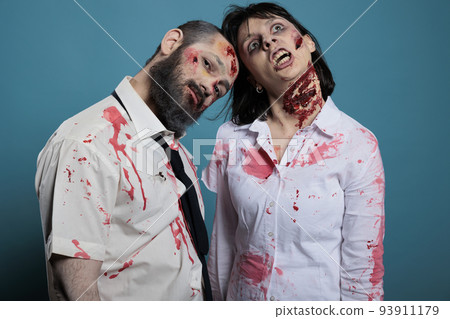Portrait of zombies couple posing on camera, looking undead and creepy with bloody wounds or ugly scars. Apocalyptic monsters with dirty scratches acting dangerous and aggressive. 93911179