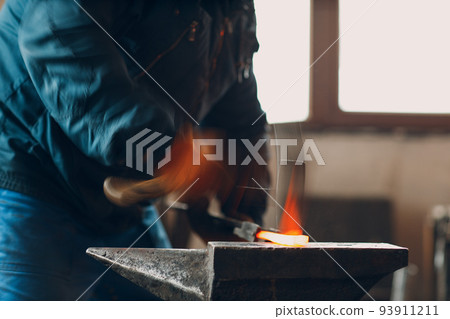 Blacksmith forges and makes metal detail with hammer and anvil at forge. Motion blur Blacksmith forges and makes metal detail with hammer and anvil at forge. Motion blur 93911211