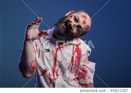 Spooky halloween zombie looking crazy evil, having blood on shirt and dangerous aggressive bloody look. Eerie apocalyptic corpse with ugly dirty scars and wounds, brain eating demon. Spooky halloween zombie looking crazy evil, having blood on shirt and dangerous aggressive bloody look. Eerie apocalyptic corpse with ugly dirty scars and wounds, brain eating demon. 93911307