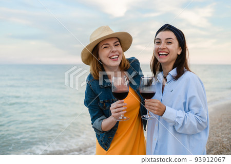 Two pretty young women with glasses of red wine by the sea. 93912067