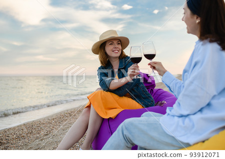 Two pretty young women with glasses of red wine by the sea. Two pretty young women with glasses of red wine by the sea. 93912071