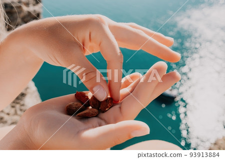 Young milky almond nuts in womans hand. A young caucasian woman eating fresh almond after morning fitness yoga near sea. Only hands are visibly. Healthy vegan food. Young milky almond nuts in womans hand. A young caucasian woman eating fresh almond after morning fitness yoga near sea. Only hands are visibly. Healthy vegan food. 93913884