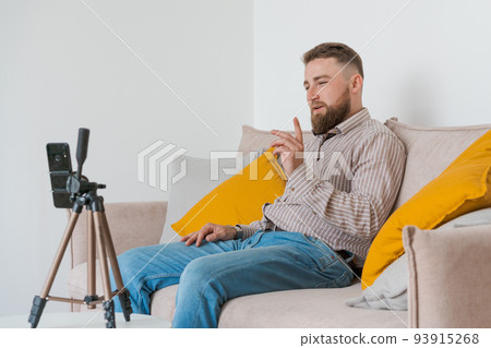Smiling bearded guy filming video using smartphone on tripod online while Smiling bearded guy filming video using smartphone on tripod online while 93915268