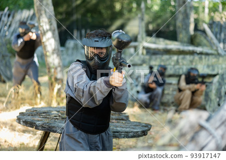 Woman in protective clothes and helmet aiming with paintball marker Woman in protective clothes and helmet aiming with paintball marker 93917147