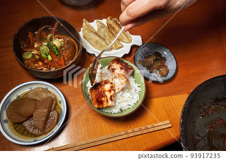 Hand with a spoon puts a piece of salmon fillet into a bowl of rice at a Japanese diner with many bowls Hand with a spoon puts a piece of salmon fillet into a bowl of rice at a Japanese diner with many bowls 93917235