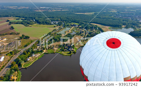 Aerial view over lake with mills and buildings on shore looking at top of flying balloon 93917242