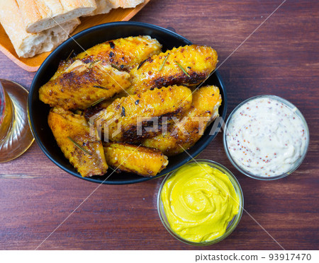 Dish of tasty fried chicken wings served in black bowl, two sauses Dish of tasty fried chicken wings served in black bowl, two sauses 93917470
