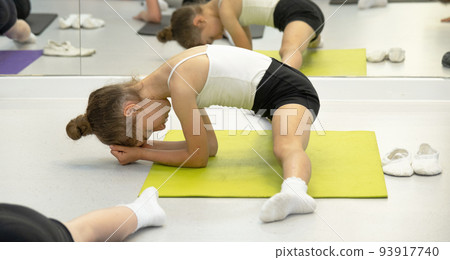 The child trains in the dance studio in the hall on the mat, does stretching exercises and abs, sits on the splits. Working on yourself and your body since childhood, overcoming yourself 93917740