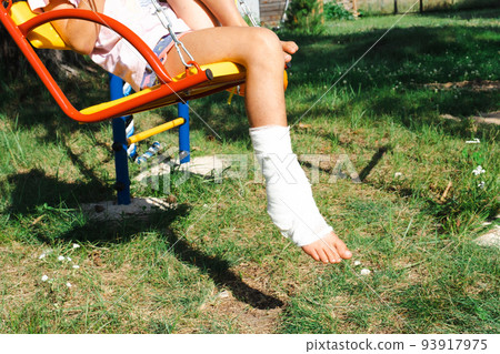 Children's legs are bandaged in plaster - barefoot on a swing. Traumatic equipment, child injury, bruise, sprain, fracture Children's legs are bandaged in plaster - barefoot on a swing. Traumatic equipment, child injury, bruise, sprain, fracture 93917975