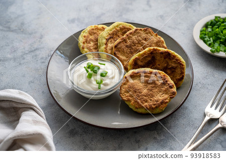 Zucchini fritters, stack of vegetarian zucchini pancakes in a plate, with fresh herbs and sour cream. 93918583