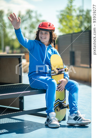 Smiling pleased skateboarder in a protective helmet waving at somebody 93919277