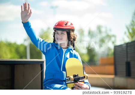 Contented adolescent skateboarder greeting somebody from the distance 93919278