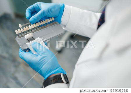 The dentist holds in hand the veneer enamel color palette and chooses the color of the tooth in the dental office. 93919918