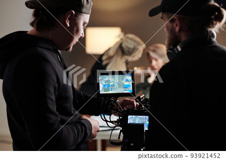 Two young men in black shirts adjusting focus of camera during shooting Two young men in black shirts adjusting focus of camera during shooting 93921452