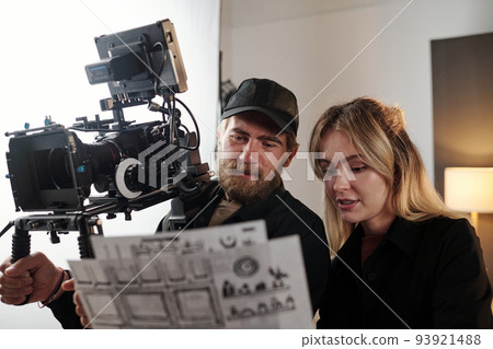 Bearded videographer and his blond female assistant discussing documents 93921488