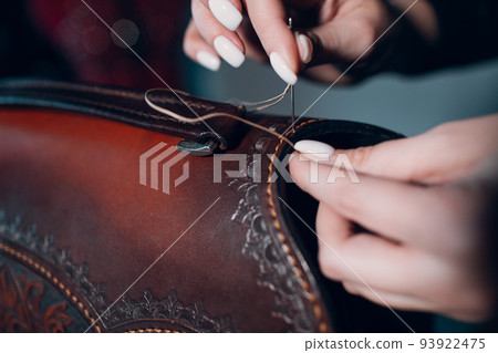 Tanner woman making sewing bag with pattern leather goods on workshop. Working process of leather craftsman. Tanner woman making sewing bag with pattern leather goods on workshop. Working process of leather craftsman. 93922475