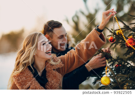 Young adult couple decorates christmas tree in winter park wood fir forest. New year pine holiday party celebration concept. 93922505
