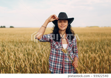 Woman american farmer wearing cowboy hat, plaid shirt and jeans at wheat field. Woman american farmer wearing cowboy hat, plaid shirt and jeans at wheat field. 93922540