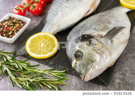 Fresh fish dorado on black slate cutting board and grey concrete background with ingredients for cooking 93923426