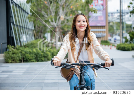Happy Asian young woman riding bicycle on street outdoor near building city 93923685