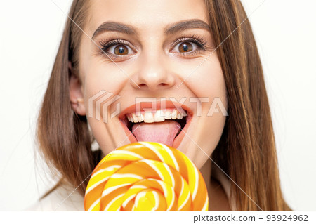 Beautiful young caucasian woman wearing a white shirt licking a lollipop on a white background 93924962