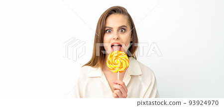 Beautiful young caucasian woman wearing a white shirt licking a lollipop on a white background Beautiful young caucasian woman wearing a white shirt licking a lollipop on a white background 93924970