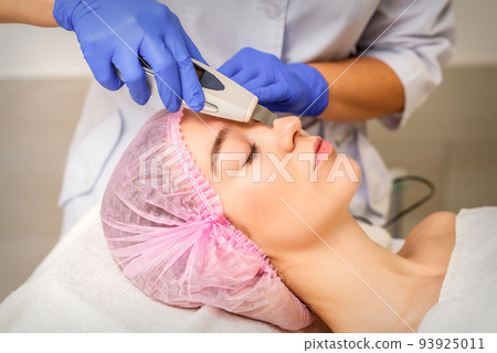 Young caucasian woman receiving facial skin cleaning by ultrasonic cosmetology face equipment in a medical salon Young caucasian woman receiving facial skin cleaning by ultrasonic cosmetology face equipment in a medical salon 93925011