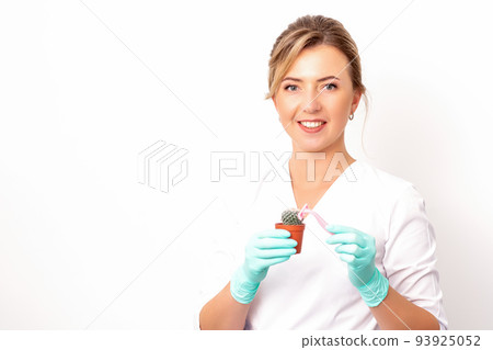 A smiling female beautician holds little green cactus with the razor in her hands. Hair removal concept 93925052