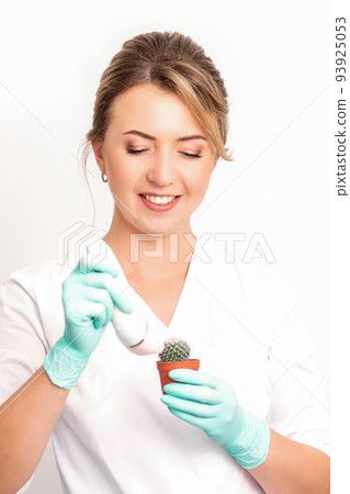 A smiling female beautician holds little green cactus with the razor in her hands. Hair removal concept A smiling female beautician holds little green cactus with the razor in her hands. Hair removal concept 93925053