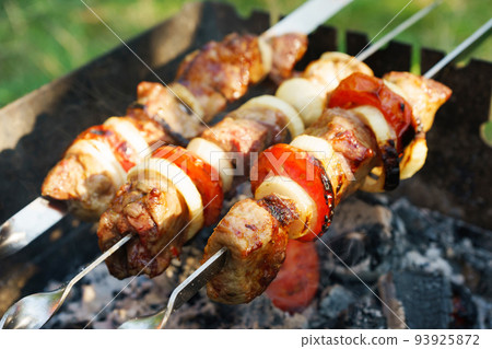 Kebab, pieces of meat on metal skewers, cooked on grill fire 93925872