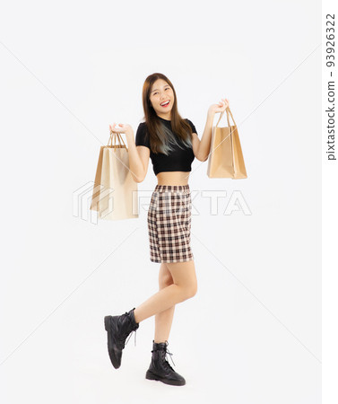 happy asian woman in black crop top t-shirt striped skirt and ankle boots carrying brown paper shopping bags on white background, full body. happy asian woman in black crop top t-shirt striped skirt and ankle boots carrying brown paper shopping bags on white background, full body. 93926322