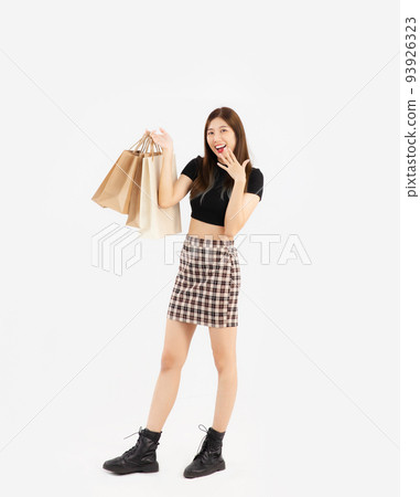 Young asian woman in black crop top t-shirt striped skirt and ankle boots carrying brown paper shopping bags posing surprised on white background, full body. Young asian woman in black crop top t-shirt striped skirt and ankle boots carrying brown paper shopping bags posing surprised on white background, full body. 93926323