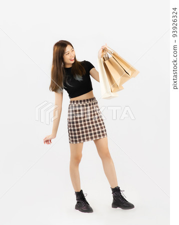 Young asian woman in black crop top t-shirt striped skirt and ankle boots carrying brown paper shopping bags on white background, full body. Young asian woman in black crop top t-shirt striped skirt and ankle boots carrying brown paper shopping bags on white background, full body. 93926324