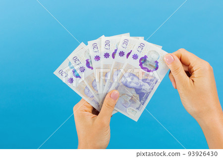 Image woman's hands which holds British pounds in her hands isolated over blue studio background. 93926430