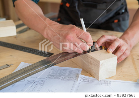 A carpenter measures wooden planks and makes marks with a pencil in a workshop. 93927665