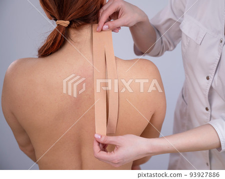 Female doctor glues kinesio tapes on the patient's shoulder. Female doctor glues kinesio tapes on the patient's shoulder. 93927886