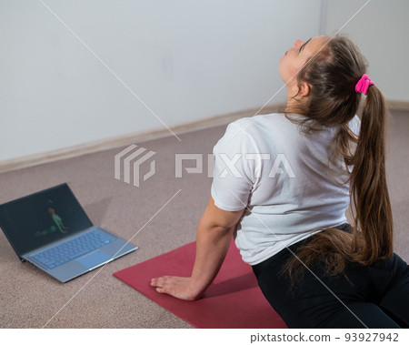 A chubby young woman is watching an online fitness lesson on a laptop. Distance sports training. A chubby young woman is watching an online fitness lesson on a laptop. Distance sports training. 93927942