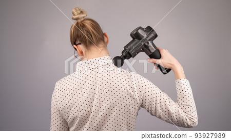 Caucasian business lady makes herself a back massage with a massager gun on a white background. Caucasian business lady makes herself a back massage with a massager gun on a white background. 93927989