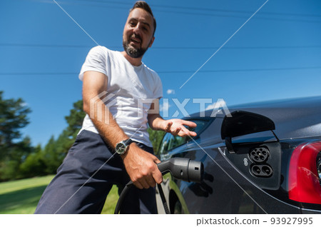 Caucasian man connect charger to electric car.  93927995