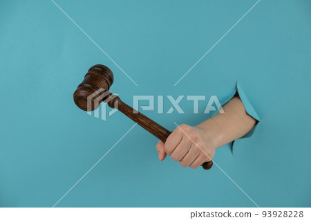 A woman's hand with a wooden judge's gavel sticks out of a hole in a blue background. A woman's hand with a wooden judge's gavel sticks out of a hole in a blue background. 93928228