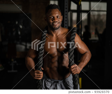 Muscular african american man posing with rope in gym. Muscular african american man posing with rope in gym. 93928370