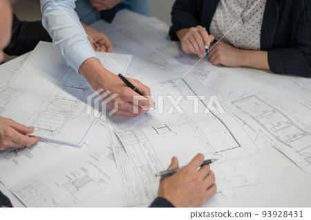 Close-up of the hands of four colleagues with blueprints on the table in the office. Brainstorming of engineers and architects. Close-up of the hands of four colleagues with blueprints on the table in the office. Brainstorming of engineers and architects. 93928431