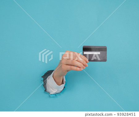 A woman's hand sticking out of a hole in a paper blue background holds a credit card.  93928451