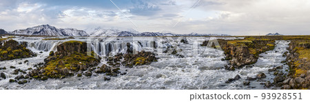 Season changing in southern Highlands of Iceland. Picturesque waterfal Tungnaarfellsfoss panoramic autumn view. Landmannalaugar mountains under snow cover in far. Season changing in southern Highlands of Iceland. Picturesque waterfal Tungnaarfellsfoss panoramic autumn view. Landmannalaugar mountains under snow cover in far. 93928551