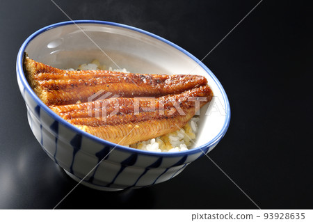 A hot eel bowl with grilled eel on top of white rice, photographed against a black background A hot eel bowl with grilled eel on top of white rice, photographed against a black background 93928635