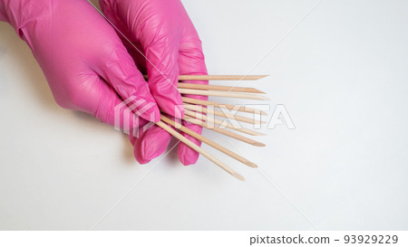 Master in pink gloves holds orange sticks for manicure.  93929229