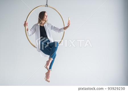Caucasian woman gymnast on an aerial hoop takes a selfie on a smartphone.  93929230