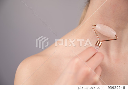 Close-up portrait of a woman using a quartz roller massager for an alternative fight against wrinkles on her neck. Smoothing of the rings of venus. Close-up portrait of a woman using a quartz roller massager for an alternative fight against wrinkles on her neck. Smoothing of the rings of venus. 93929246