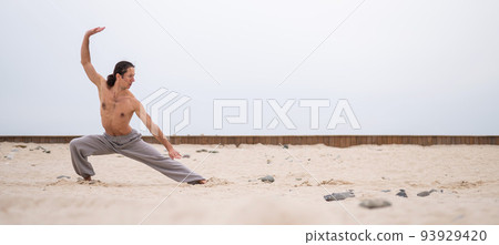 Caucasian man with long hair practicing qigong outdoors.  93929420